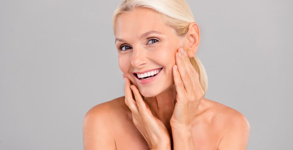 Portrait of positive retired lady touch face enjoy perfect skin after beauty product balm isolated on grey color background